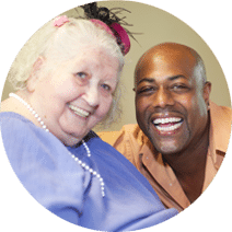 a smiling elderly female with a smiling male caregiver